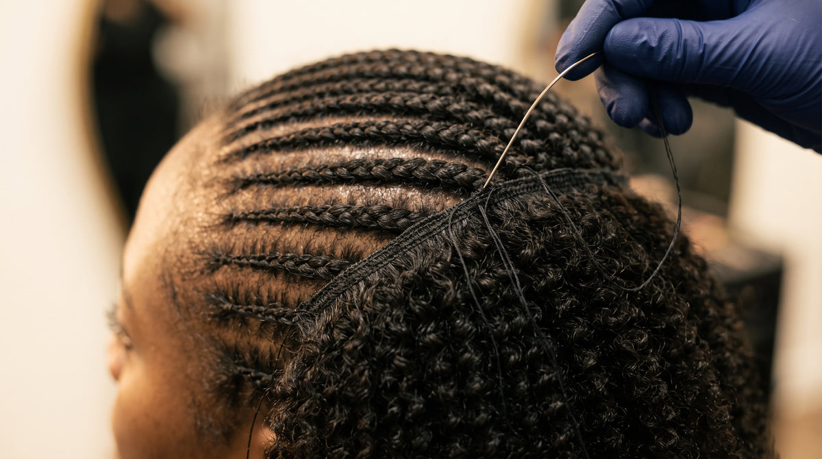 A weft being sewn onto cornrow braids during a sew-in install