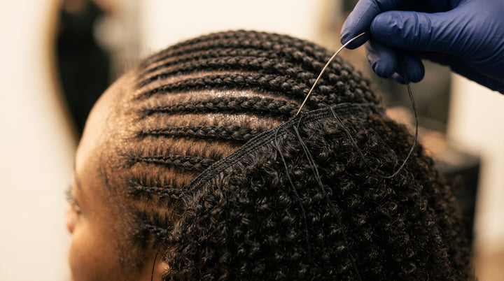 A weft being sewn onto cornrow braids during a sew-in install